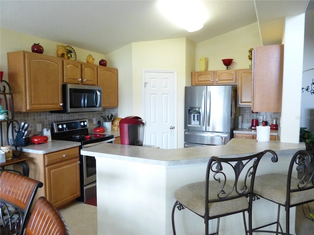 kitchen with kitchen peninsula, appliances with stainless steel finishes, backsplash, and a breakfast bar area