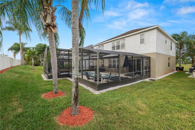 back of property with glass enclosure, a yard, and a pool