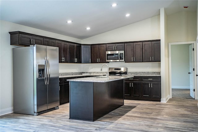 kitchen with dark brown cabinetry, a center island with sink, light stone counters, stainless steel appliances, and light wood-type flooring