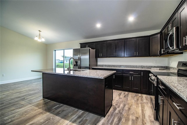 kitchen featuring appliances with stainless steel finishes, light stone counters, a kitchen island with sink, light wood-style floors, and a sink