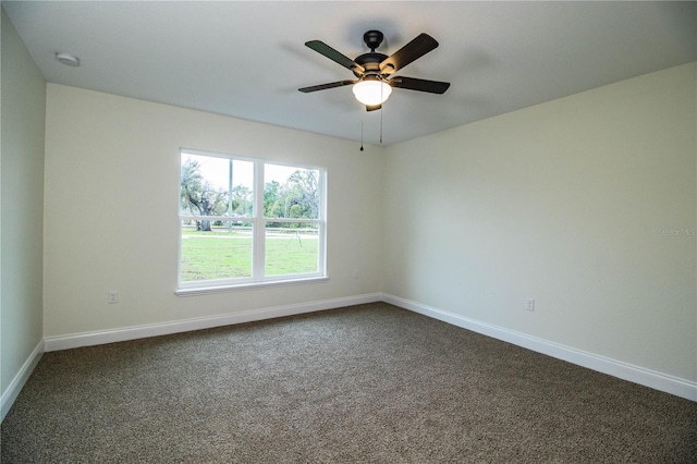 spare room featuring dark colored carpet, a ceiling fan, and baseboards