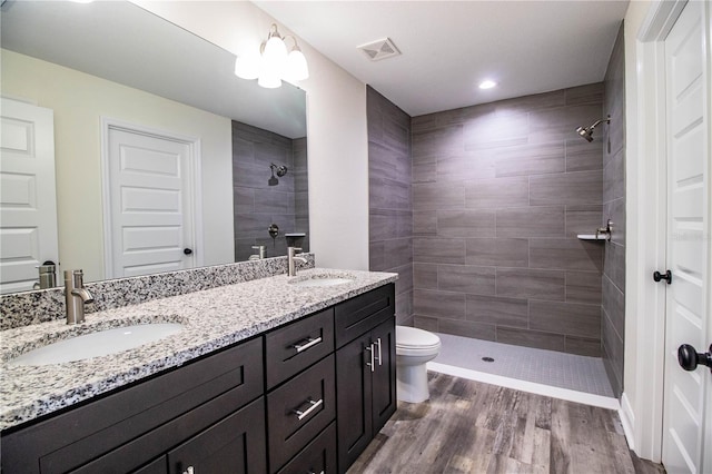 full bath featuring visible vents, wood finished floors, a sink, and tiled shower