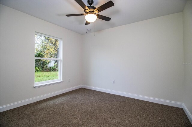 spare room featuring a ceiling fan, plenty of natural light, dark carpet, and baseboards