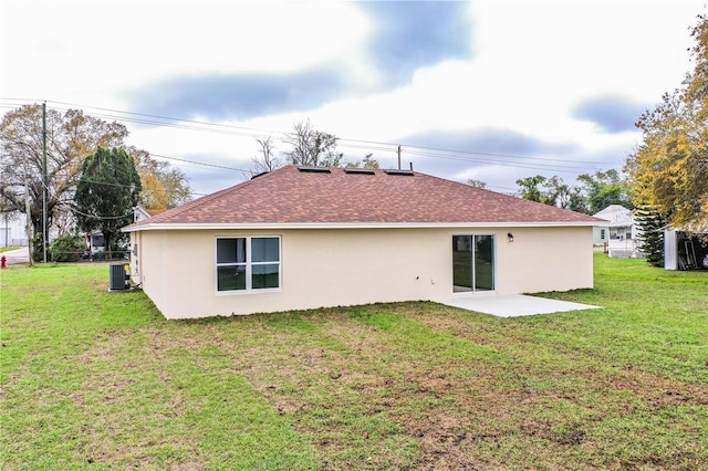 rear view of house featuring a shingled roof, stucco siding, a yard, and central air condition unit