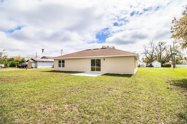 rear view of property featuring roof with shingles, a patio area, a lawn, and stucco siding