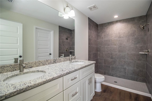 full bath with wood finished floors, tiled shower, a sink, and visible vents