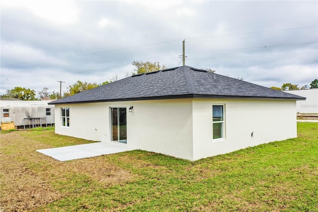 back of property with a shingled roof, a lawn, and stucco siding