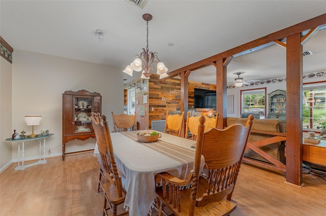 dining space with wooden walls, light hardwood / wood-style flooring, and ceiling fan with notable chandelier