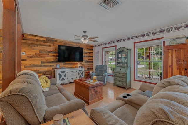 living room featuring light hardwood / wood-style flooring, ceiling fan, and wooden walls