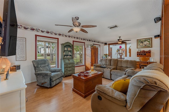 living room with ceiling fan, a textured ceiling, and light hardwood / wood-style flooring