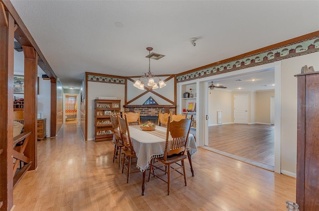 dining room featuring ceiling fan with notable chandelier, a brick fireplace, light hardwood / wood-style flooring, built in features, and ornamental molding