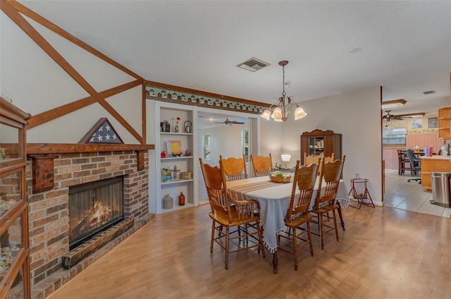 dining area featuring ceiling fan with notable chandelier, built in features, a fireplace, and light hardwood / wood-style flooring