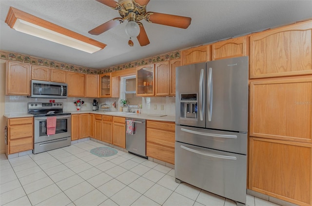 kitchen with appliances with stainless steel finishes, backsplash, ceiling fan, sink, and light tile patterned floors