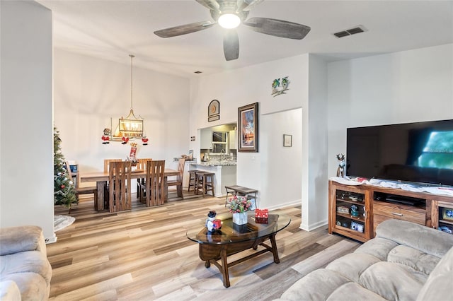 living room featuring ceiling fan with notable chandelier and light hardwood / wood-style floors