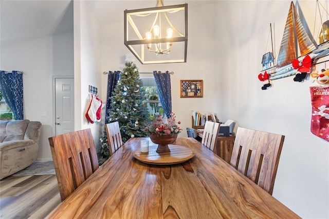 dining space with hardwood / wood-style floors, vaulted ceiling, and an inviting chandelier