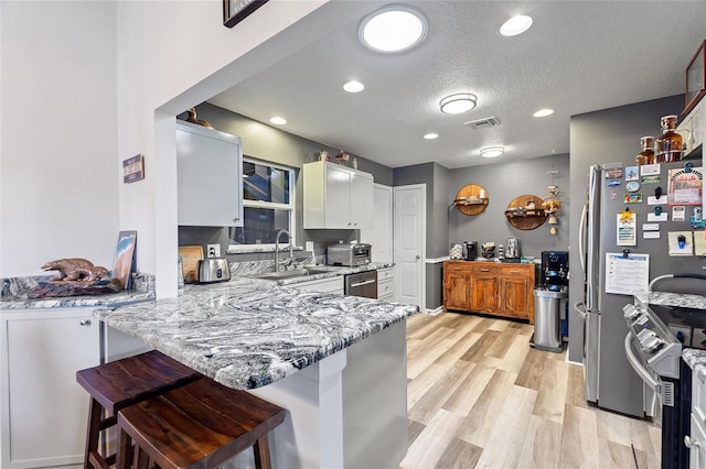 kitchen with kitchen peninsula, a kitchen bar, light wood-type flooring, sink, and white cabinetry