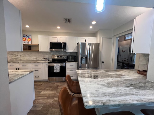 kitchen with a kitchen bar, white cabinets, dark hardwood / wood-style flooring, light stone counters, and stainless steel appliances