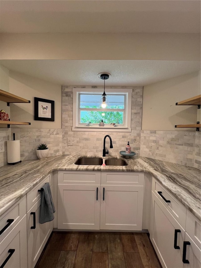 kitchen with white cabinetry, sink, hanging light fixtures, light stone counters, and dark hardwood / wood-style floors