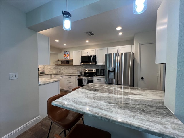 kitchen featuring light stone countertops, white cabinetry, stainless steel appliances, kitchen peninsula, and decorative backsplash