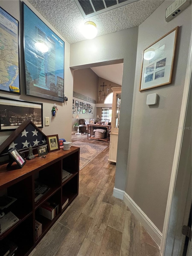 hallway featuring a textured ceiling, hardwood / wood-style flooring, and vaulted ceiling