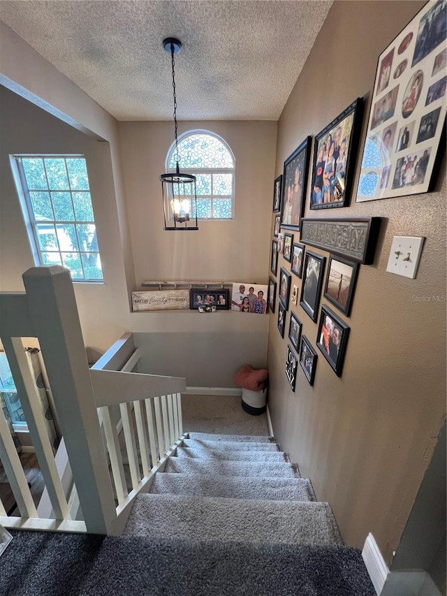 stairway featuring carpet flooring, a textured ceiling, and a chandelier