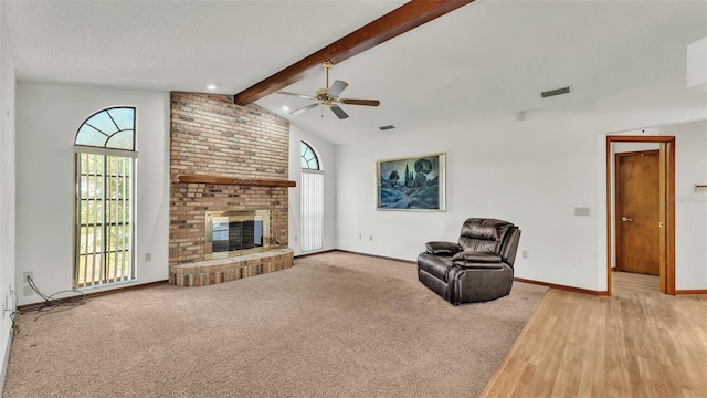 unfurnished living room featuring ceiling fan, a brick fireplace, vaulted ceiling with beams, light hardwood / wood-style flooring, and a textured ceiling