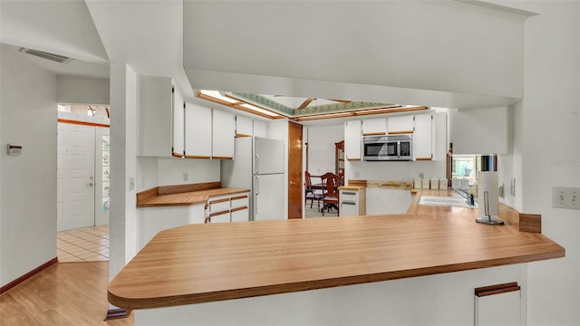 kitchen with white cabinets, white refrigerator, sink, light hardwood / wood-style floors, and kitchen peninsula