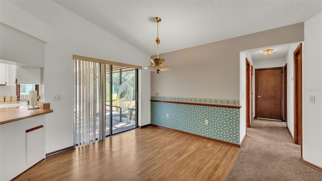 unfurnished dining area with a textured ceiling, light hardwood / wood-style flooring, and vaulted ceiling