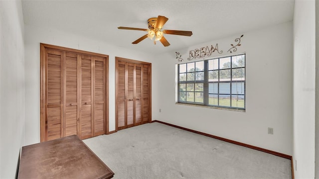 unfurnished bedroom featuring carpet flooring, ceiling fan, and multiple closets