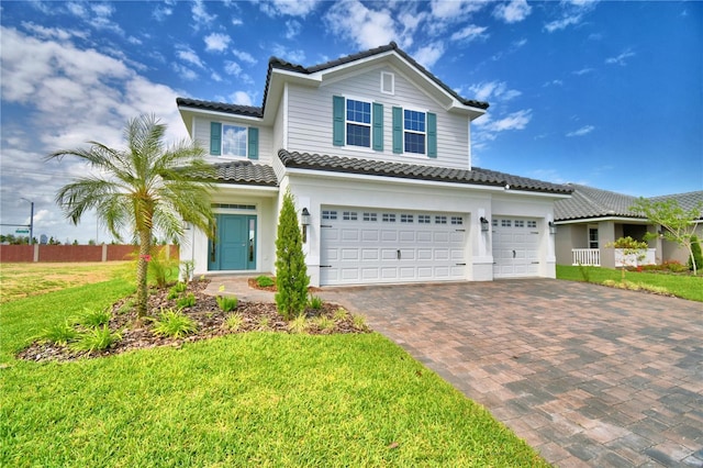 traditional home featuring a front yard, a tile roof, a garage, and decorative driveway