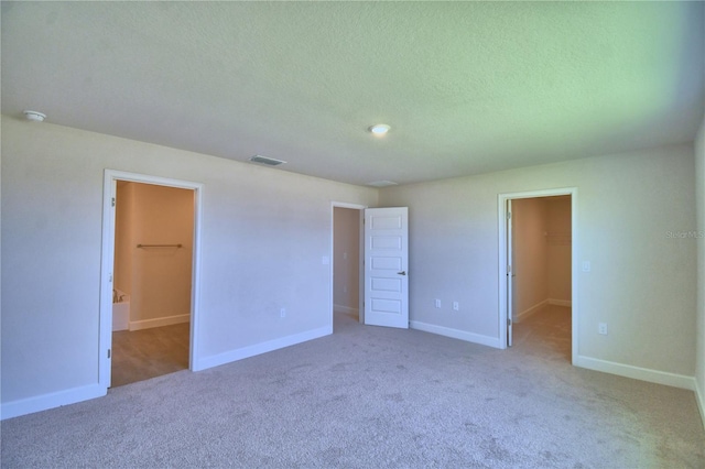 unfurnished bedroom featuring a closet, a textured ceiling, carpet floors, a walk in closet, and visible vents
