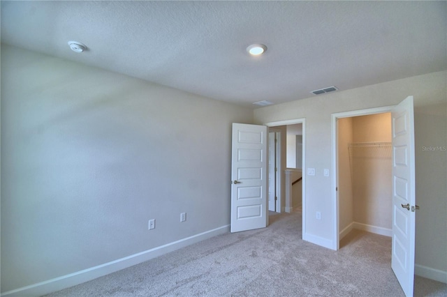 unfurnished bedroom with a closet, visible vents, carpet flooring, a walk in closet, and baseboards