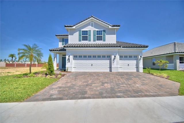 traditional-style home featuring a tiled roof, decorative driveway, a front yard, fence, and a garage