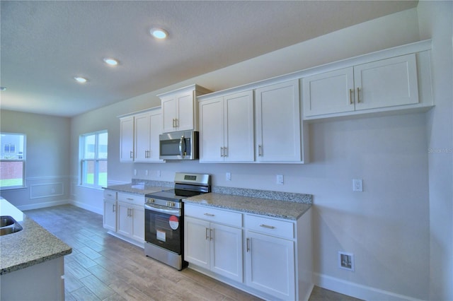 kitchen with light wood-style flooring, white cabinets, recessed lighting, a wainscoted wall, and stainless steel appliances