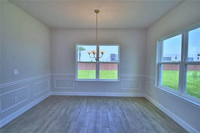 unfurnished dining area featuring an inviting chandelier, wainscoting, and dark wood finished floors