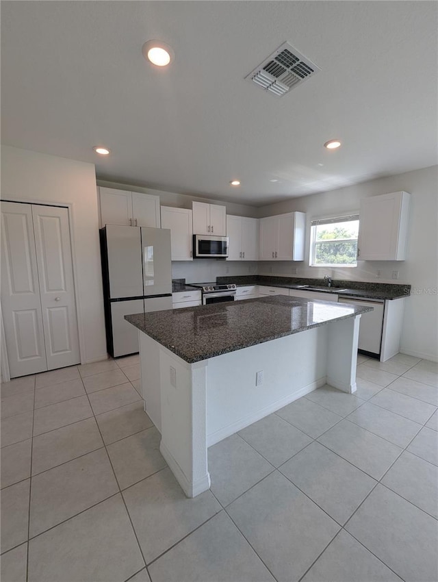 kitchen with light tile patterned floors, a kitchen island, dark stone counters, white cabinets, and appliances with stainless steel finishes