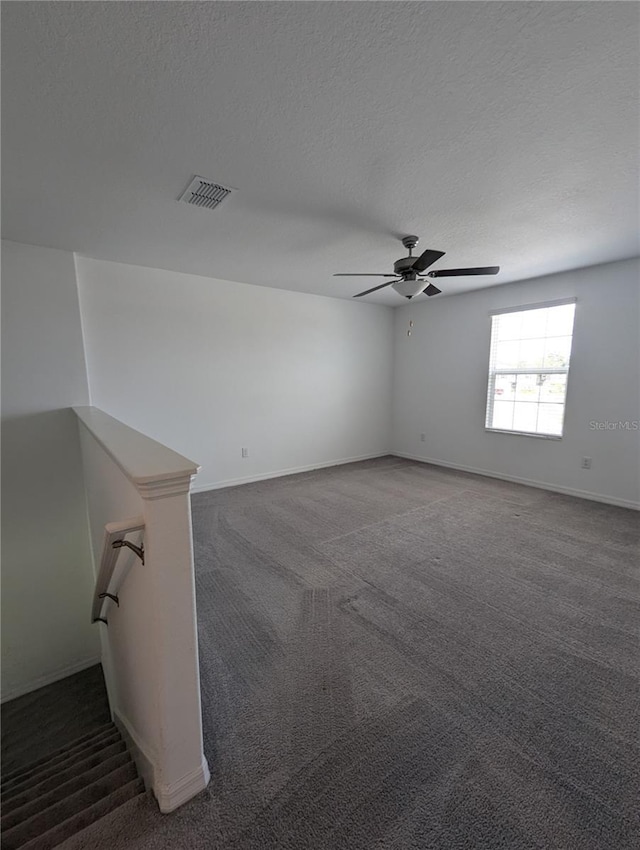 empty room featuring dark colored carpet, ceiling fan, and a textured ceiling