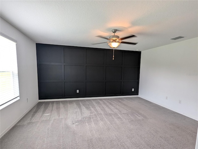 carpeted spare room featuring a textured ceiling, a wealth of natural light, and ceiling fan