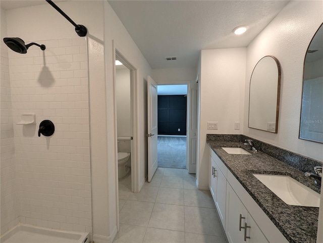 bathroom with tile patterned floors, vanity, a tile shower, and toilet