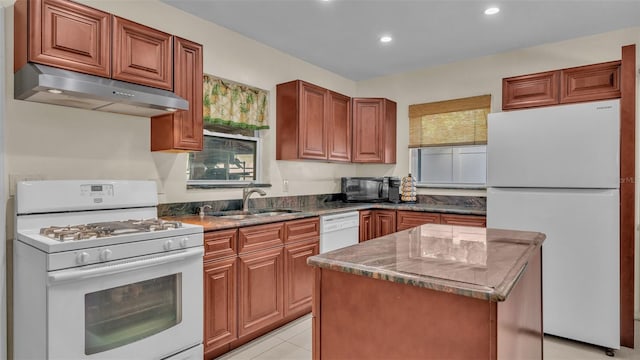 kitchen featuring white appliances, sink, dark stone countertops, light tile patterned floors, and a kitchen island