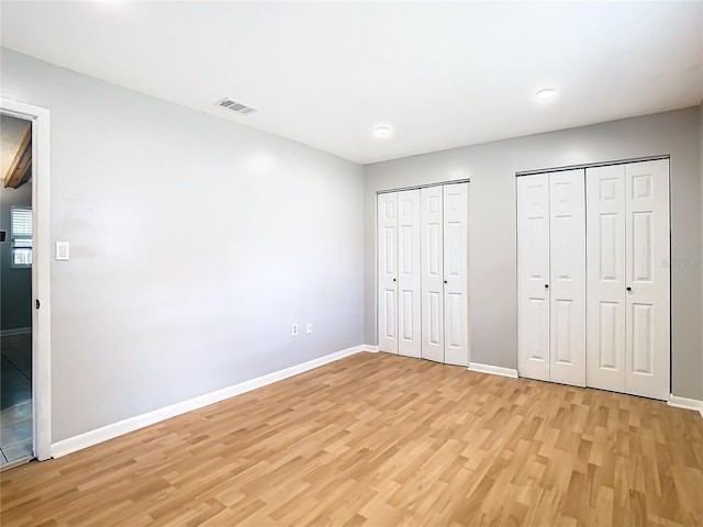 unfurnished bedroom featuring light hardwood / wood-style floors and multiple closets