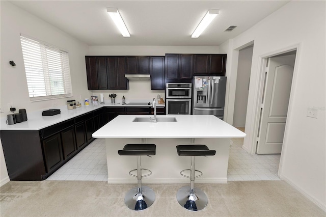 kitchen with a kitchen bar, stainless steel appliances, light colored carpet, sink, and a center island with sink