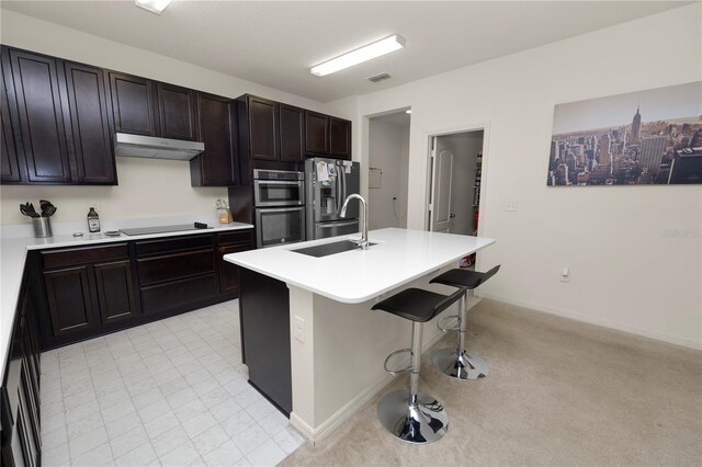 kitchen featuring sink, light carpet, a breakfast bar area, a kitchen island with sink, and appliances with stainless steel finishes