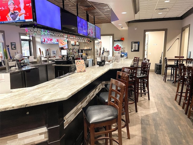 bar with light stone counters, ornamental molding, and light hardwood / wood-style flooring