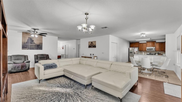 living room with ceiling fan with notable chandelier, dark wood-type flooring, and a textured ceiling