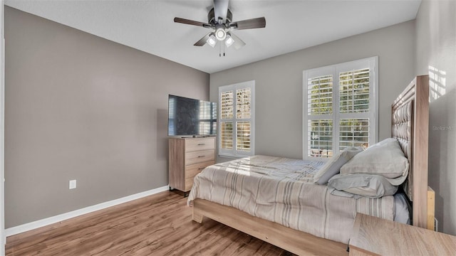 bedroom featuring multiple windows, a ceiling fan, baseboards, and wood finished floors