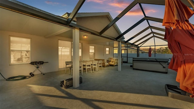 patio terrace at dusk featuring glass enclosure and a hot tub