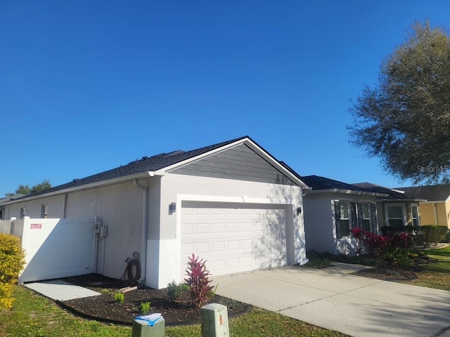 view of side of property featuring stucco siding, driveway, an attached garage, and fence