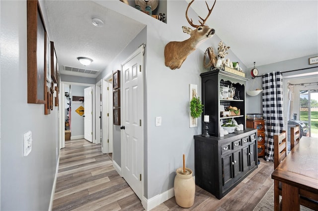 hallway featuring lofted ceiling, wood-type flooring, and a textured ceiling