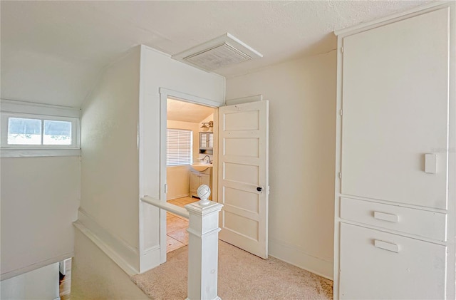 hallway with sink, light colored carpet, and vaulted ceiling